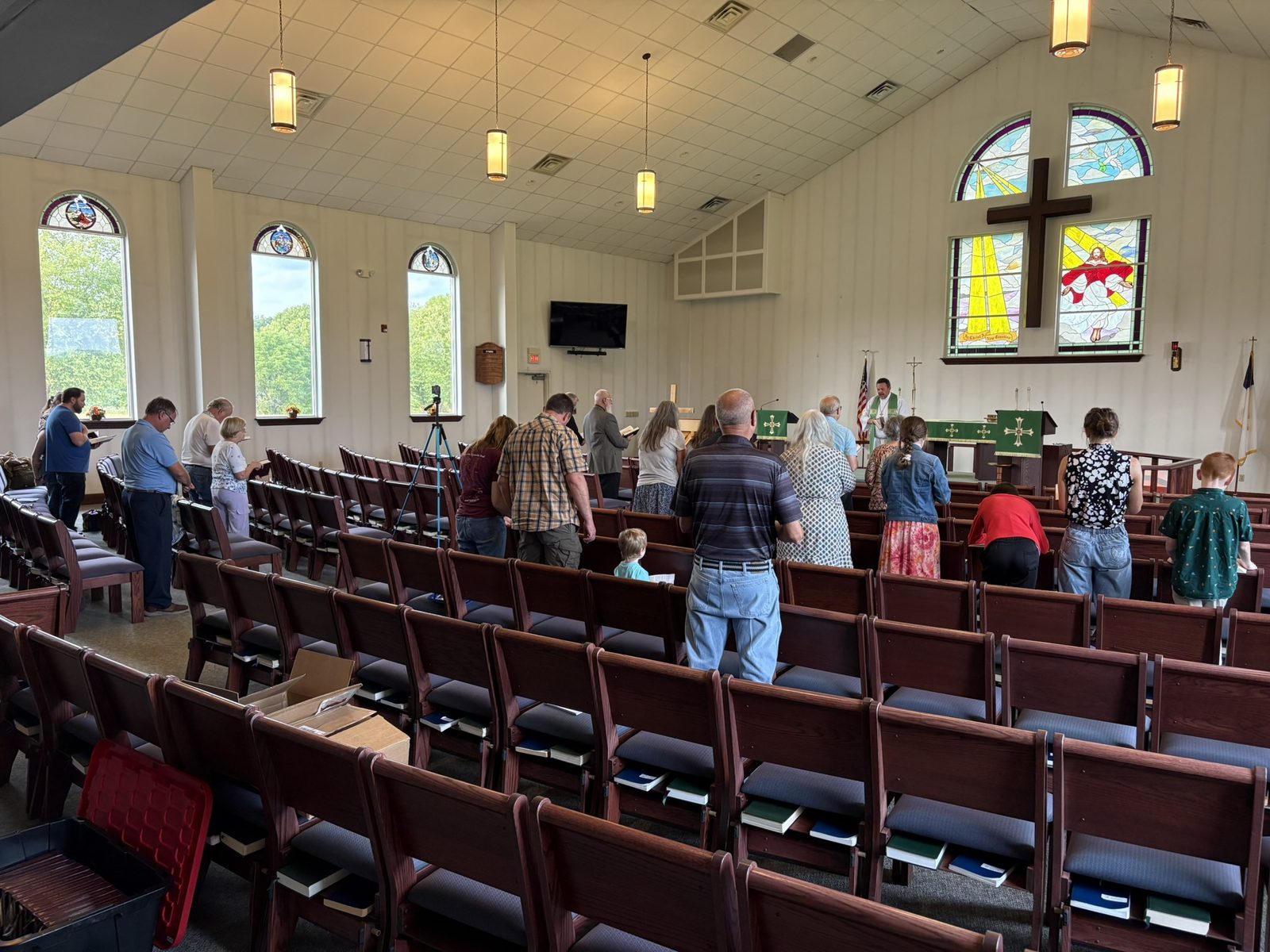 The people of Gallipolis Lutheran Mission standing in worship before a wooden cross and stained glass windows.